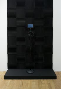 Gary Hill Whisper Room, 2022 Video (color, sound), acoustic paneling, 7” HD industrial flat panel display, microphone stand, headphones, media player with activation switch Dimensions variable, portrait orientation 3 min 10 sec Edition of 2, 1 AP